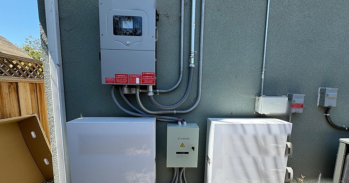Outdoor battery installation with inverter, safety labels and two white LFP battery cabinets